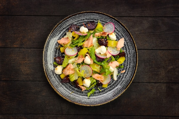 Bovenaanzicht van salade met zalm, radijs, courgette en rode biet op houten tafel