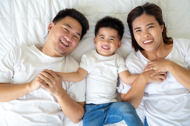 Bovenaanzicht van schattige kleine jongen en zijn Aziatische ouders camera kijken en glimlachen