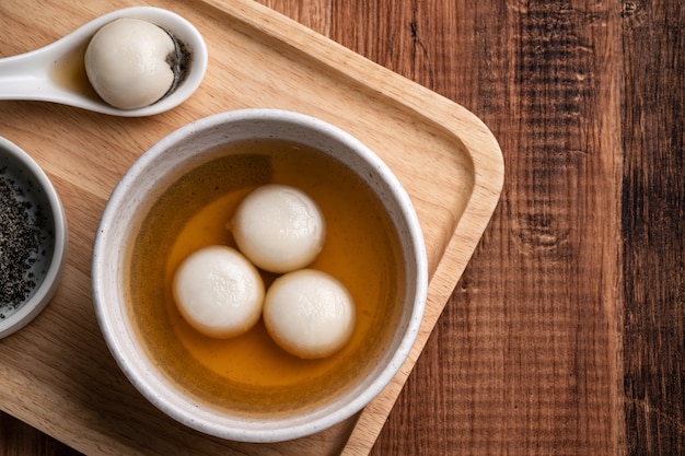 Bovenaanzicht van sesam grote tangyuan (tang yuan, kleverige rijst knoedel ballen) met zoete siroop soep in een kom op houten tafel achtergrond voor winterzonnewende festival voedsel.