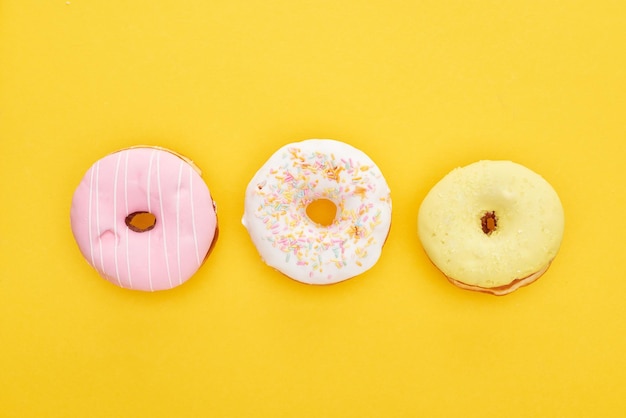 Bovenaanzicht van smakelijke kleurrijke geglazuurde donuts op felgele achtergrond