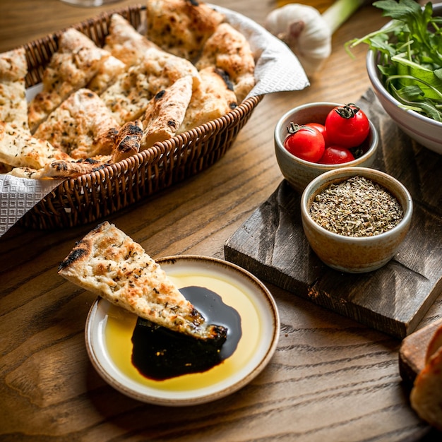 Bovenaanzicht van sneetjes brood in mand gedoopt sneetje brood om wat tomaten en tijm in kleine kom op houten tafel te oliën