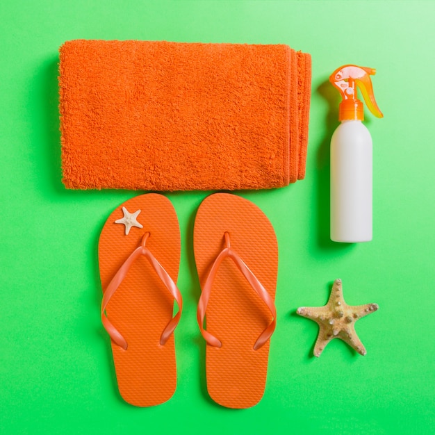 Bovenaanzicht van strand plat lag accessoires. zonnebrandcrème fles met schelpen, zeester, handdoek en flip-flop op gekleurde achtergrond met kopie ruimte.