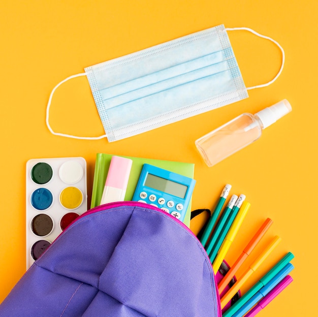 Foto bovenaanzicht van terug naar school essentials met rugzak en medisch masker