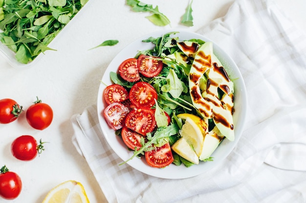 Bovenaanzicht van tomatensalade rucola avocado citroen in witte plaat op lichte achtergrond