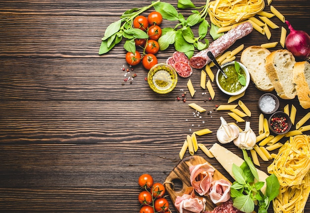 Bovenaanzicht van traditionele Italiaanse gerechten, hapjes en snacks als salami, prosciutto, kaas, pesto, ciabatta, olijfolie, pasta op rustieke houten achtergrond