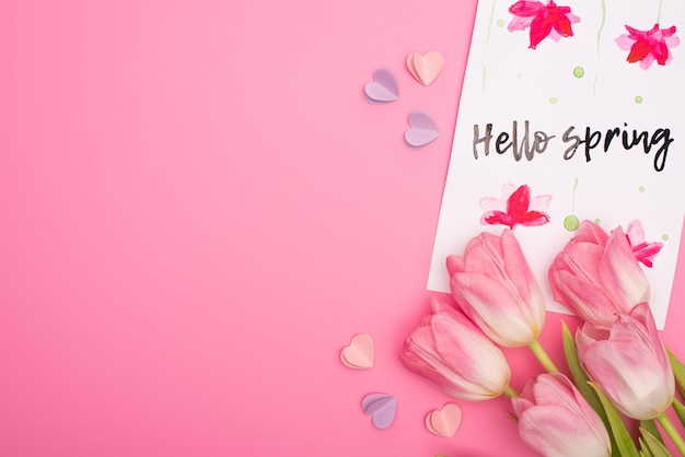 Bovenaanzicht van tulpenkaart met hallo lente-letters en kleurrijke decoratieve hartjes op roze