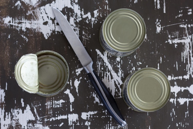 Bovenaanzicht van twee gesloten blikjes en één open blikje met mes op de houten ondergrond