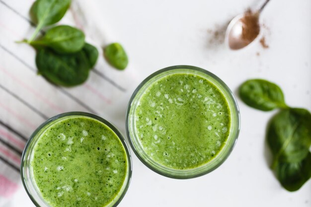 Bovenaanzicht van twee groene spinaziecocktails en verse groenten op de achtergrond