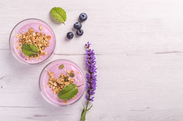 Foto bovenaanzicht van twee kommen bessenyoghurt met muesli en haver voor een gezond ontbijt op een rustieke witte tafel