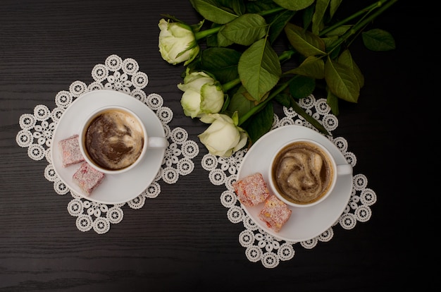 Bovenaanzicht van twee kopjes koffie met melk, Turks fruit op een schoteltje, witte rozen