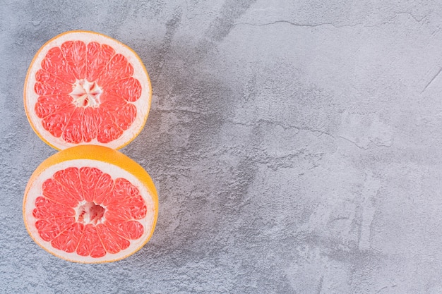Bovenaanzicht van twee plakjes verse grapefruit op grijs.