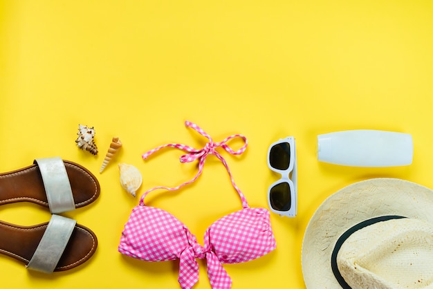 Bovenaanzicht van twee stukken roze zwemkleding en strand accessoties op gele achtergrond.