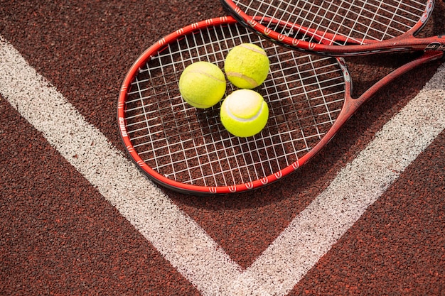 Bovenaanzicht van twee tennisrackets en drie gele ballen liggen door witte lijnen te kruisen