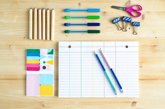 Bovenaanzicht van vel papier met lijnen omgeven door groep potloden en kleurpotloden met clips, schaar en set gummen