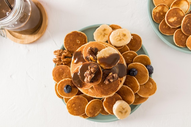 Bovenaanzicht van vele kleine pannenkoeken en dikke pannenkoeken met chocoladepasta op een keramische plaat Banaan schijfjes noten heerlijk ontbijt