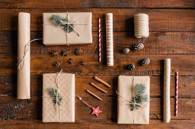 Bovenaanzicht van verpakte en verpakte geschenkdozen, opgerold papier, dennenappels, decoraties, draden, kaneel en steranijs op houten tafel