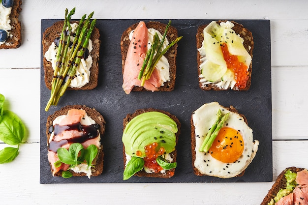 Bovenaanzicht van verschillende bruschettas, sandwiches met verschillende gezonde fillihgs geserveerd op een donkere plaat