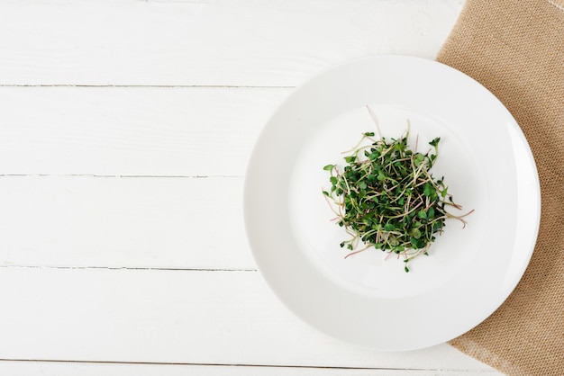 Bovenaanzicht van verse microgreen op plaat op beige servet op wit houten oppervlak