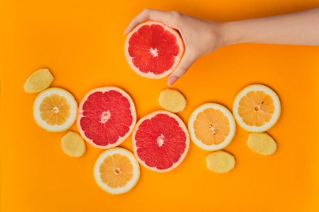 Bovenaanzicht van verse plakjes citroen, grapefruit en gember op fel oranje achtergrond