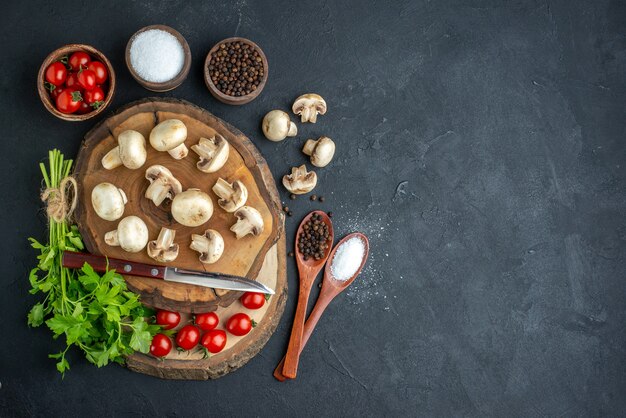 Bovenaanzicht van verse rauwe champignons en groene bundel mes tomaten kruiden op houten plank handdoek op zwarte achtergrond