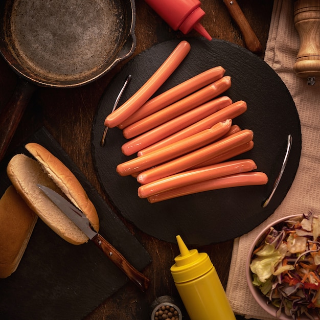 Bovenaanzicht van verse worstjes voor hotdogs op donker met broodjes.