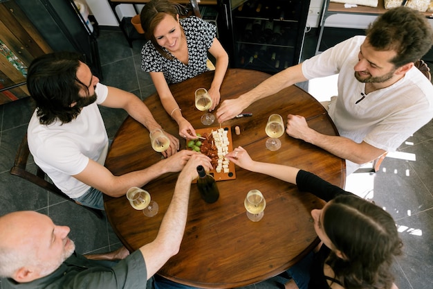 Bovenaanzicht van vrienden rond de tafel met witte wijn en tapashapjes