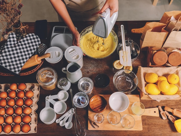 Bovenaanzicht van vrouw die zelfgemaakte bakkerij bereidt in een keuken thuis, veel bakingrediënten op tafel