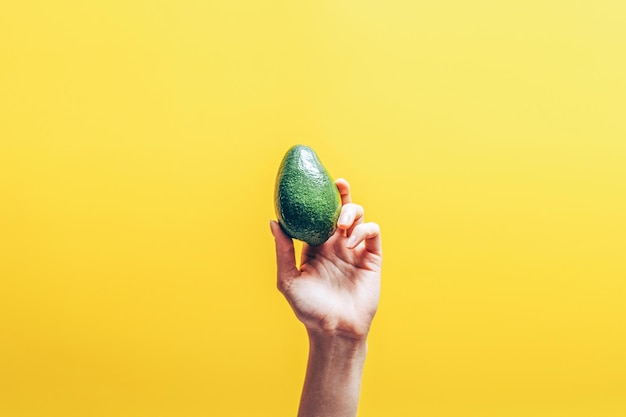 Bovenaanzicht van vrouw hand met avocado op gele achtergrond