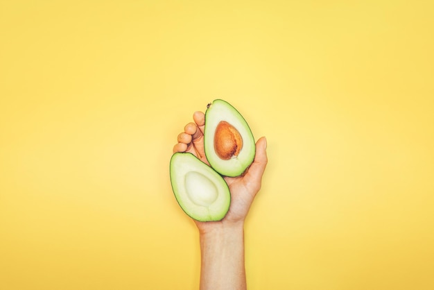 Bovenaanzicht van vrouw hand met avocado op gele achtergrond