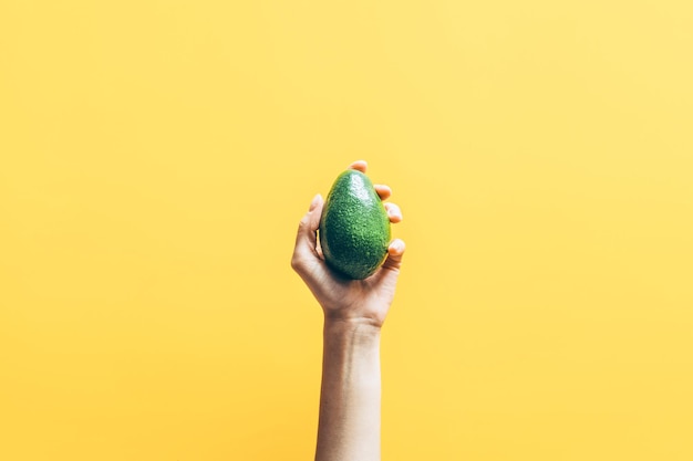 Bovenaanzicht van vrouw hand met avocado op gele achtergrond