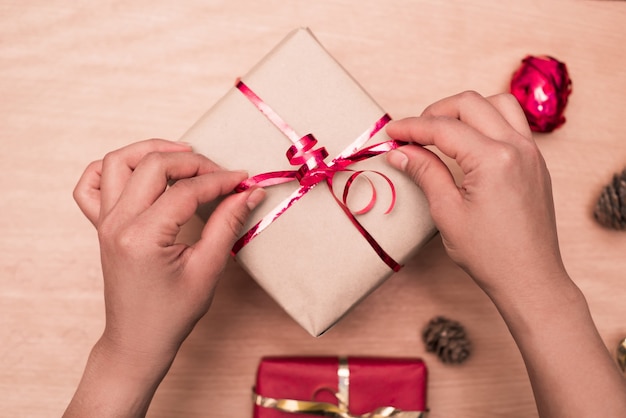 Bovenaanzicht van vrouw handen koppelverkoop rood lint op handgemaakte aanwezig op houten tafel, pakket voor kerstcadeaus.