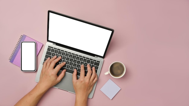 Bovenaanzicht van vrouw handen typen op laptopcomputer met slimme telefoon en koffiekopje op roze achtergrond