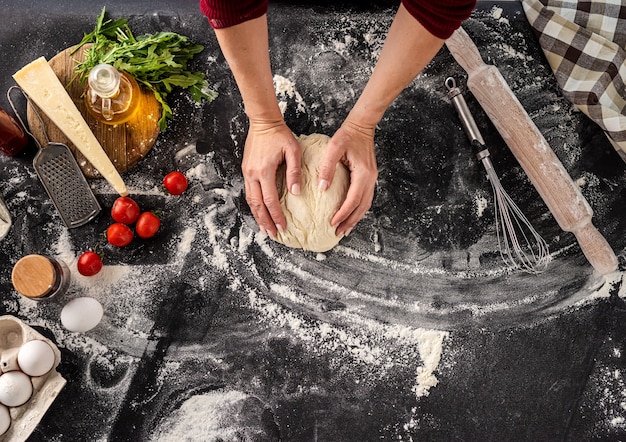 Foto bovenaanzicht van vrouw kneden van deeg voor pizza bakken op zwarte met bloem bestoven achtergrond