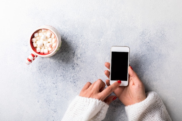 Bovenaanzicht van vrouw met smartphone en kopje met marshmallows