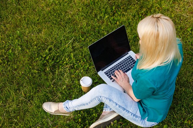 Bovenaanzicht van vrouw zitten in park op het groene gras met laptop, handen op toetsenbord. Computerschermmodel. Student die buiten studeert. Ruimte voor tekst kopiëren