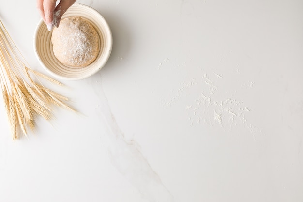 Bovenaanzicht van vrouwelijke hand gieten meel in brooddeeg in een marmer met tarwe en meel met ruimte voor tekst