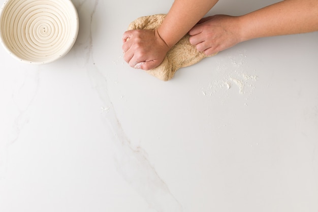 Bovenaanzicht van vrouwelijke hand kneden brooddeeg in een marmeren tafel met een lege broodkom met ruimte voor tekst