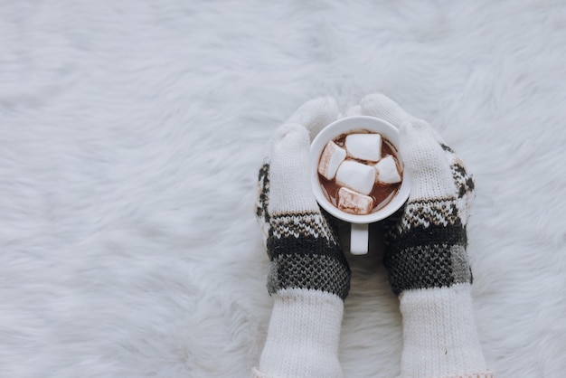 Bovenaanzicht van vrouwelijke handen in handschoenen met mok heerlijke chocolade met marshmallow op witte vacht