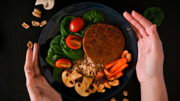 Bovenaanzicht van vrouwelijke handen met een bord veganistisch plantaardig voedsel, veganistische vleesloze kotelet en ric