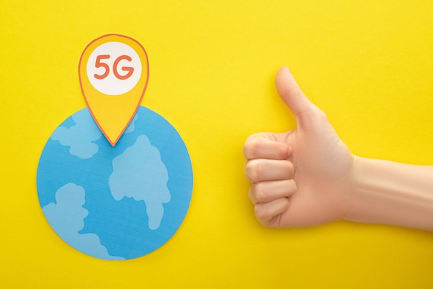 Bovenaanzicht van wereldbol en 5g-letters in locatiemarkering bij duim omhoog op gele achtergrond