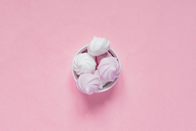 Bovenaanzicht van witte en roze gedraaide schuimgebakjes in porseleinen kom op roze