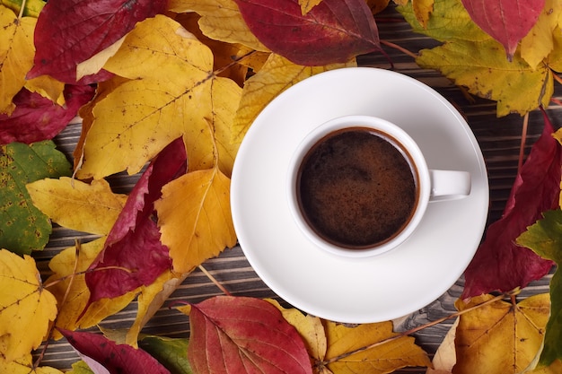 Bovenaanzicht van witte kopje koffie en herfst gele bladeren rond op houten tafel