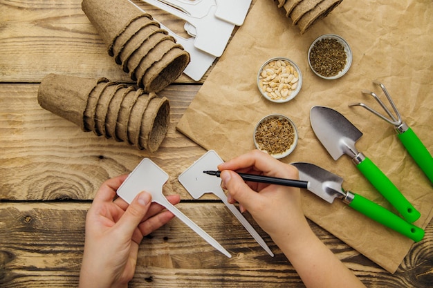 Bovenaanzicht van zaden en tuingereedschap op een houten ondergrond Womens handen ondertekenen een teken voor de plant