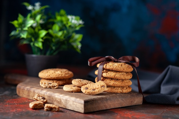 Bovenaanzicht van zelfgemaakte heerlijke suikerkoekjes op een houten bord en bloempot op een donkere achtergrond van mixkleuren