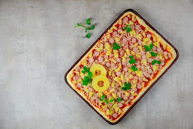 Bovenaanzicht van zelfgemaakte pizza met ananas, kaas en worst in pan.