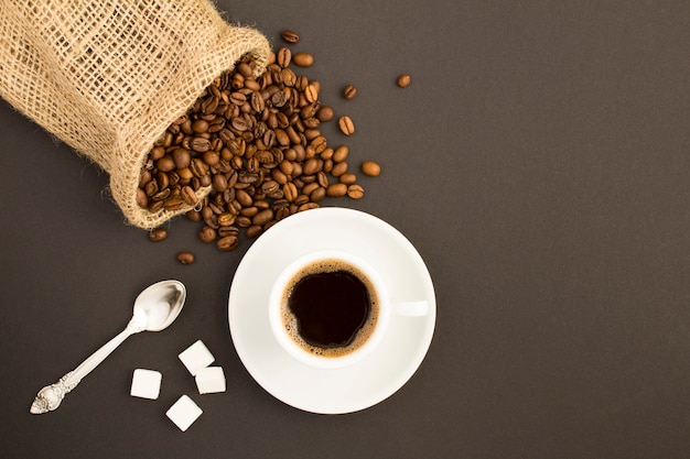 Bovenaanzicht van zwarte koffie in de witte kop en koffiebonen op de donkere achtergrond