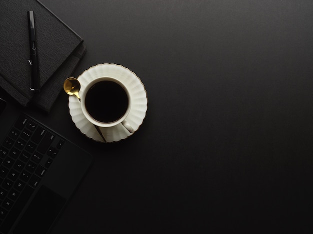 Bovenaanzicht van zwarte tafel met koffiekopje, briefpapier, laptop en kopie ruimte in kantoor aan huis