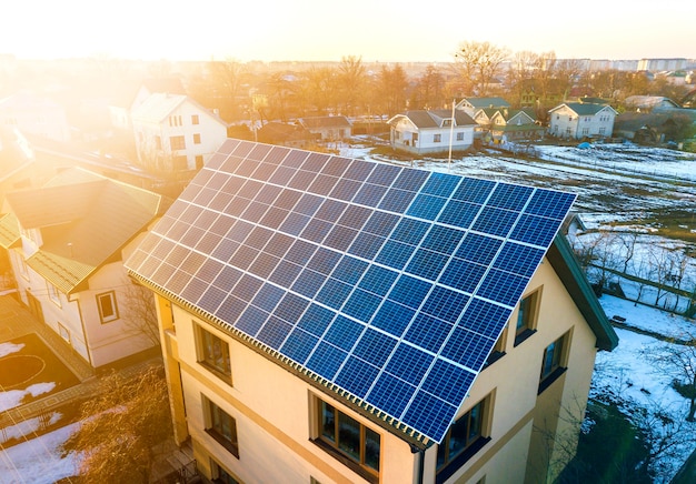 Bovenaanzicht vanuit de lucht van een nieuw, modern woonhuis met twee verdiepingen en een blauw glanzend fotovoltaïsch zonnepaneelsysteem op het dak. Hernieuwbaar ecologisch groen energieproductieconcept.