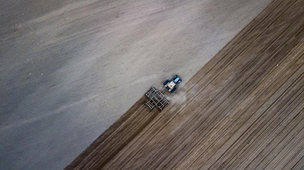 Bovenaanzicht vanuit de lucht van een tractor maaidorser die landbouwgrond ploegt in de lente