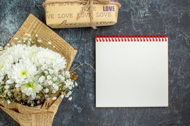 bovenaanzicht verpakte geschenken bloemen notitieboekje op donkere achtergrond